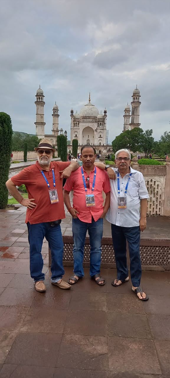 Three delegates in front of Bibi Ka Maqbara under a cloudy sky